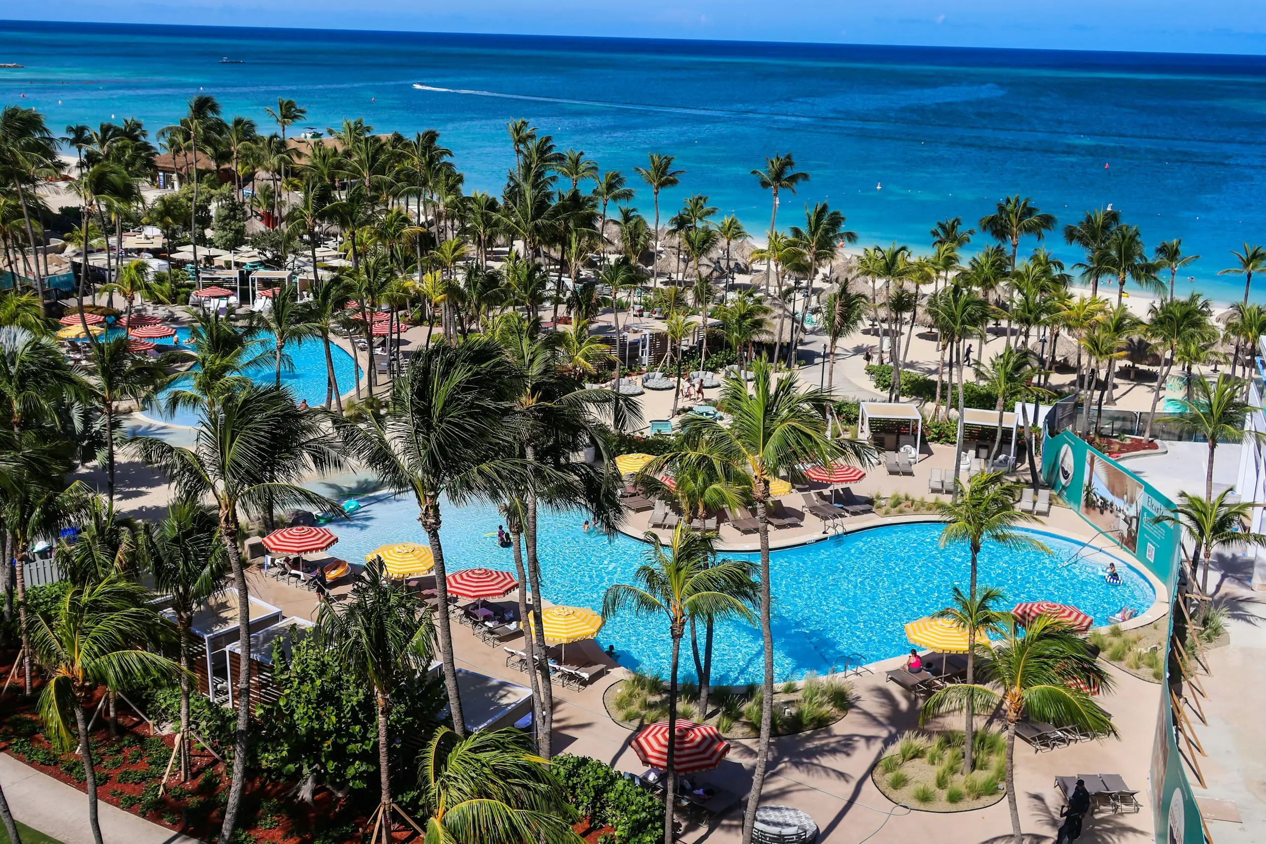 Tropical all-inclusive resort pool lined with palm trees beside the ocean