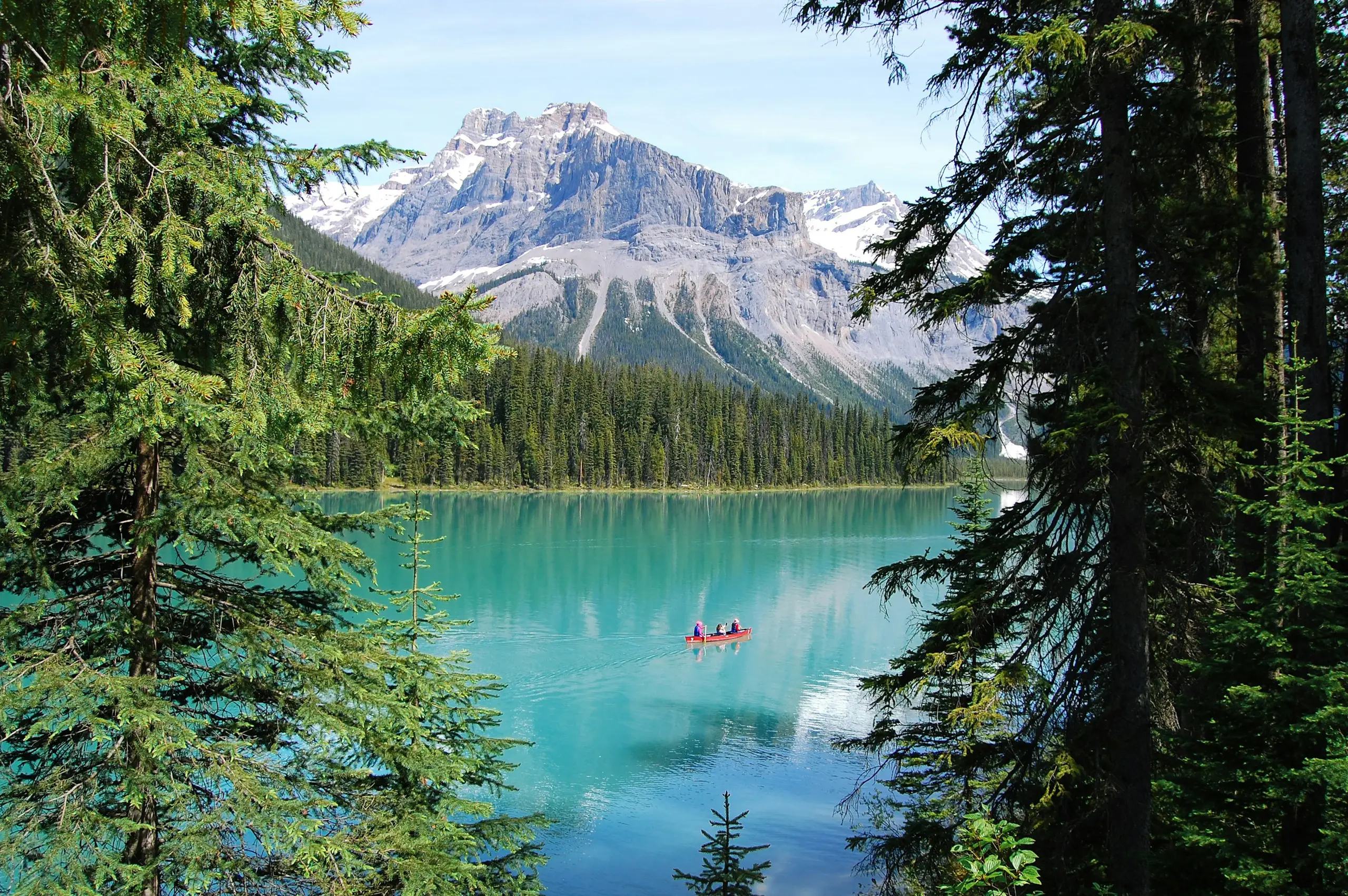 Red canoe on turquoise Banff Lake, Canada β framed by pine trees