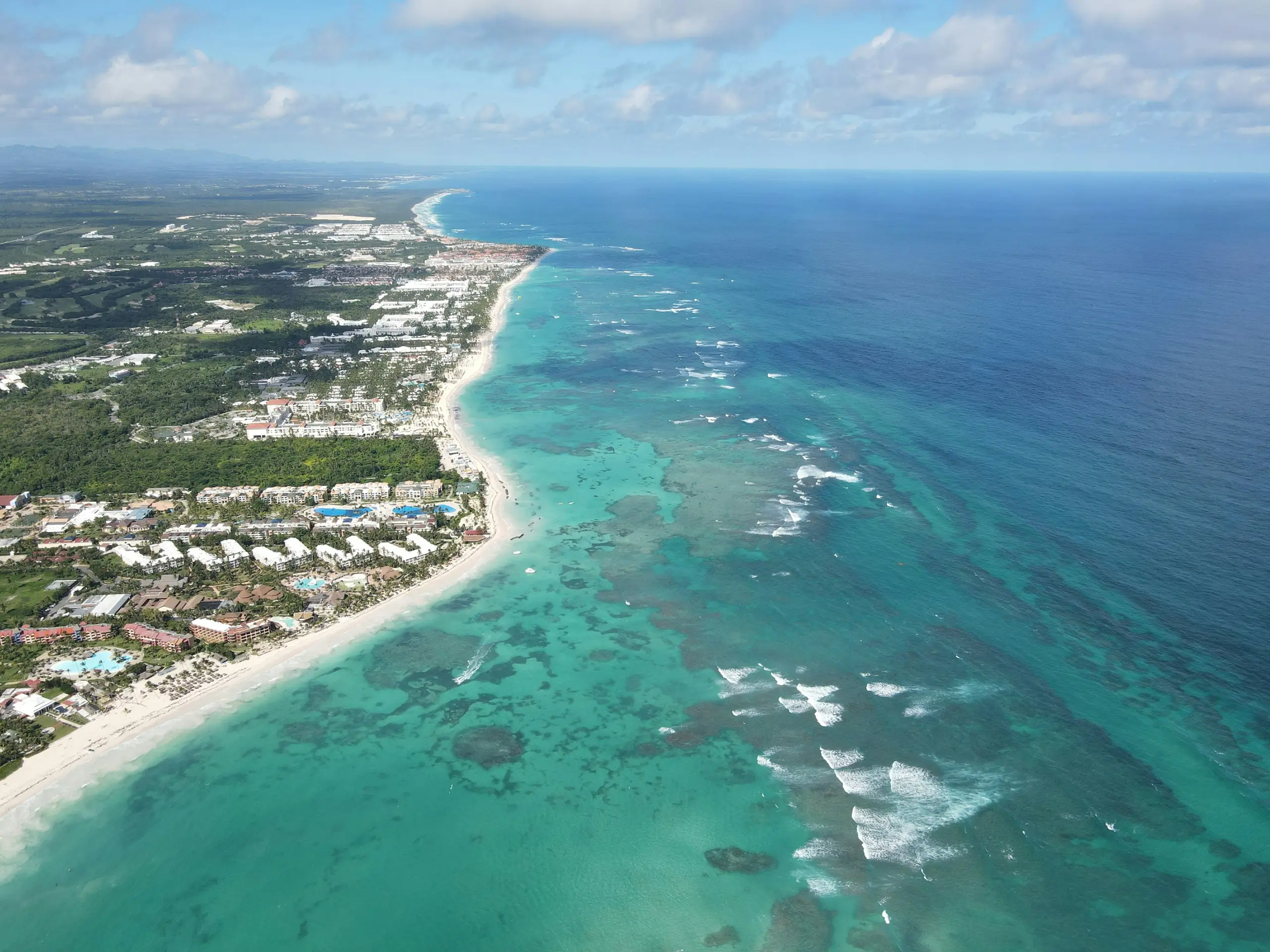 Aerial view of the Punta Cana coastline, with resorts along a white-sand beach and turquoise reef water