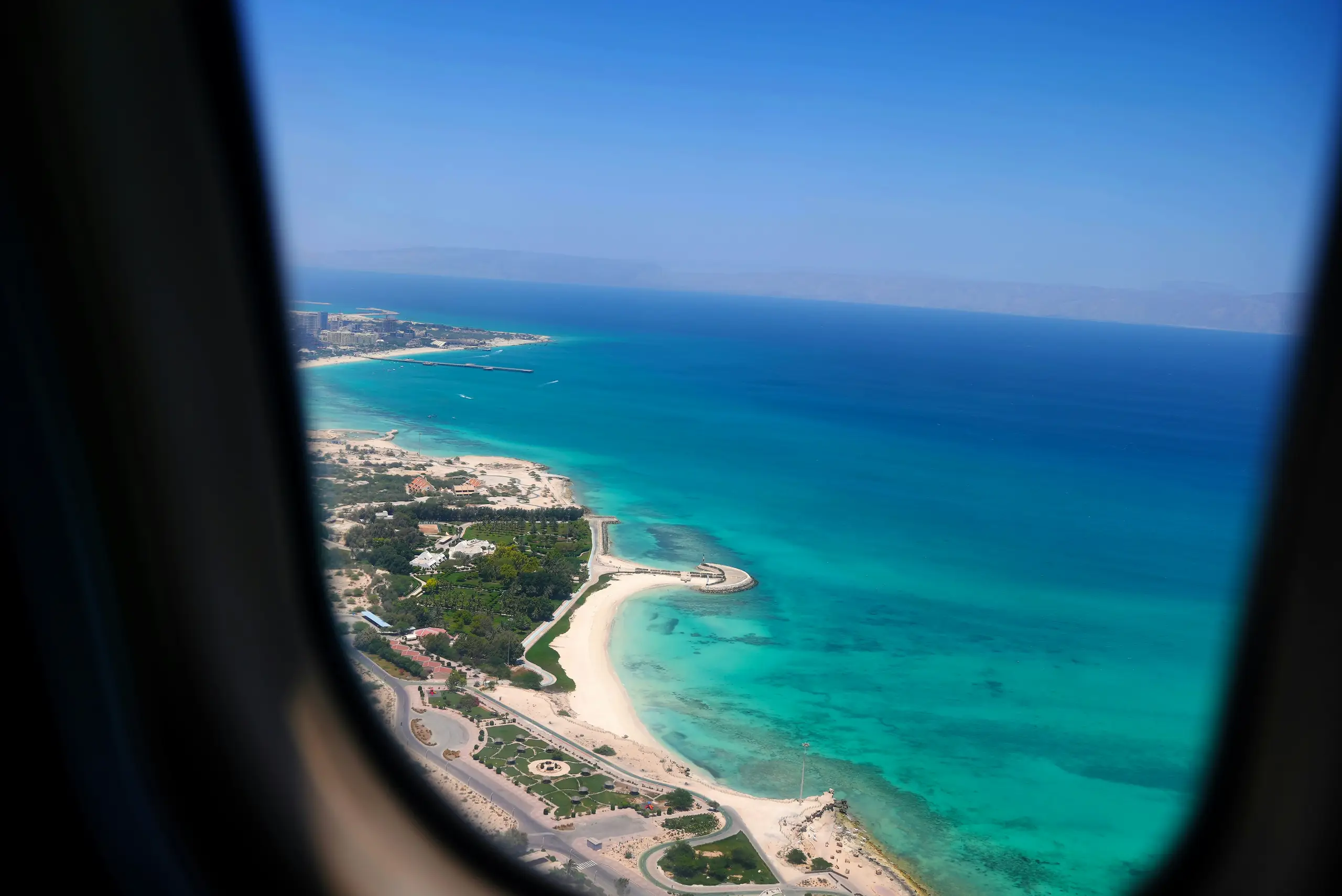 View from an aircraft window of a turquoise coastline with sandy beaches and a pier
